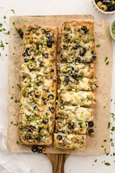 two slices of bread with olives and cheese on a cutting board next to bowls of olives