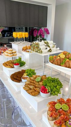 an assortment of food is displayed on a buffet table with clear chairs and bar stools