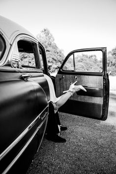 a black and white photo of a woman leaning out the window of a car