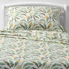 a bed with green and yellow leaves on the comforter, next to a white headboard