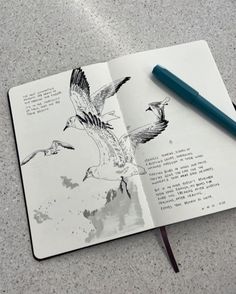 an open book with birds flying over it and a pen on the table next to it