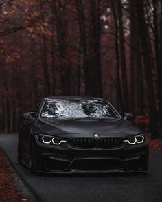 the front end of a black bmw car on a road with trees in the background