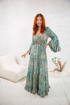 Introducing our stunning Phoebe dress, the perfect addition to any boho-inspired wardrobe. Crafted from high-quality materials, this maxi dress features a chic green allover print that's sure to turn heads. Designed with 3/4 sleeves and a flattering v-neckline, this dress is both feminine and playful. The buttons on the front and drawstring waist allow you to customize the fit to your liking, while the flutter sleeves add a touch of whimsy. Whether you're headed to a summer wedding or a beachside brunch, the Phoebe dress is the perfect choice. Dress it up with heels and statement earrings, or keep it casual with sandals and a sunhat. At Ananda Wild we're committed to creating beautiful, ethically-made pieces that you'll love wearing for years to come. Available in 3 sizes SM Length 150cm W Hippie Long Maxi Dress With Floral Print, Long Hippie Dress With Floral Print, Hippie Boho Maxi Dress With Floral Print, Hippie Floral Print Maxi Dress, Long Floral Print Boho Dress, Long Bohemian Floral Print Boho Dress, Flowy Boho Print Maxi Dress With Long Sleeves, Long Boho Dress With Floral Print In Hippie Style, Long Sleeve Boho Print Maxi Dress For Vacation