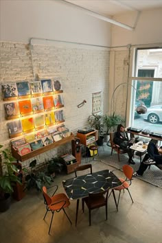 two people sitting at a table in front of a large window with pictures on the wall