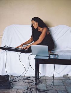 a woman sitting on top of a couch using a laptop computer next to a keyboard