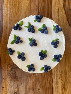 a cake with white frosting and blueberries on top sitting on a wooden table