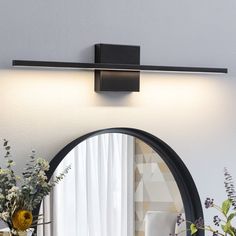 a round mirror sitting on top of a wall next to a vase with flowers