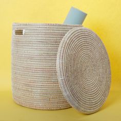 a white basket with a blue lid on it sitting next to a yellow wall,