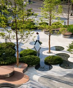 a man walking through a park with lots of trees and bushes in the middle of it