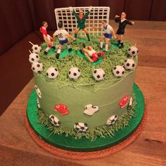 a cake decorated with soccer players on top of green grass and white net in the background