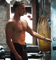 a shirtless man is standing in front of a punching bag and looking off into the distance