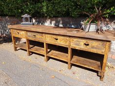 an old wooden table with two drawers and shelves on the top, sitting in front of a brick wall