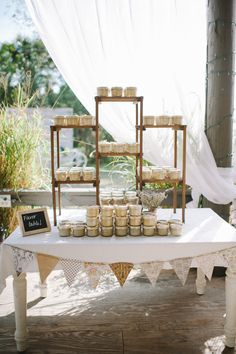 a table topped with lots of jars and cups on top of a white cloth covered table