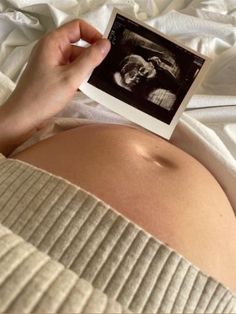 a pregnant woman laying in bed with her stomach exposed and holding an album over her belly