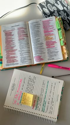 an open bible next to a notebook with sticky notes on it and a pink pen