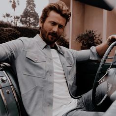 a man sitting in the driver's seat of a car with his hand on the steering wheel