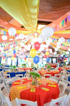 tables and chairs are set up for an event with colorful balloons hanging from the ceiling