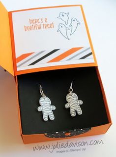 pair of earrings in gift box on white table with orange and black striped ribbon around it