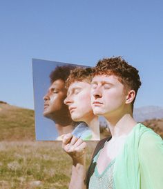 two men standing in front of a mirror with their eyes closed and one man holding his head up