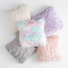 four different colored fur pillows on a white surface