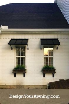 two windows with plants in them on the side of a white brick building that says design your awning com