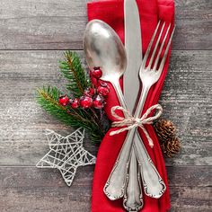 two forks and spoons wrapped in red cloth with pine cones on the side next to them