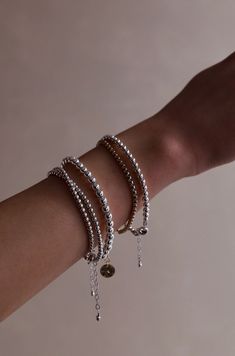 A hand with several bracelets rests against a neutral background. The bracelets are silver and gold with varying beads and chains, adding depth and texture to the wrist. Minimalist Stackable Bracelets With Round Beads, Silver Flexible Bracelet For Everyday Wear, Silver Flexible Bracelets For Everyday Wear, Everyday Flexible Silver Bracelets, Stackable Bracelets With Round Beads, Silver Stackable Beaded Bracelets For Everyday, Flexible Silver Stackable Bracelets, Trendy Stackable Wrap Bracelet With Round Beads, Trendy Silver Stretch Bracelet With Round Beads