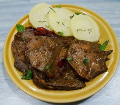 a yellow plate topped with meat and sliced up potatoes on top of a wooden table