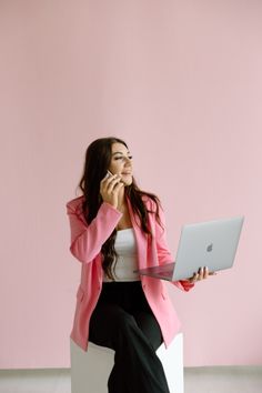 a woman sitting on a chair talking on her cell phone and holding a laptop computer