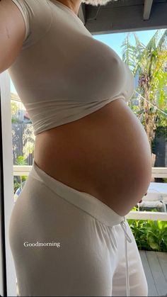 a pregnant woman wearing white shorts and a tank top is standing in front of a window