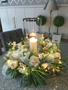 a candle is lit on top of a table with flowers and greenery in the center