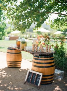 two wooden barrels with drinks on them sitting next to each other in front of a tree