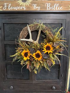 a wreath with sunflowers and antlers hangs on the front door of a house