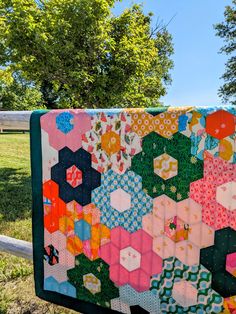 a quilt hanging on a clothes line in front of a fence with trees and grass behind it