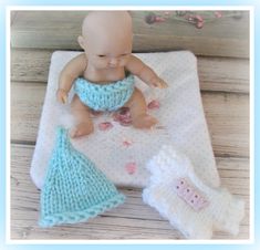 a baby doll sitting on top of a blanket next to two knitted mittens