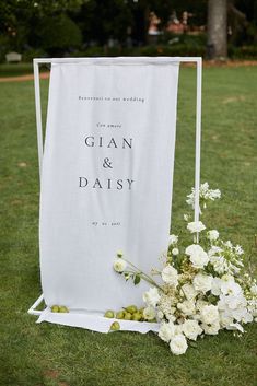 white flowers and greenery sit on the grass next to an outdoor wedding ceremony sign