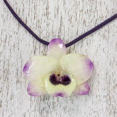 A real Dendrobium Orchid preserved in resin is showcased in this pendant necklace presented by Danai of Thailand. The orchid has pale yellow petals tipped in purple and hangs from a deep purple leather cord. Two sliding tiger's eye beads dyed purple secure the ends of the cord and allow the necklace length to be adjusted. Dendrobium Orchid, Gifts For Travelers, Yellow Petals, The Orchid, Yellow And Purple, Purple Orchids, Dope Jewelry, Flower Pendant Necklace, Funky Jewelry