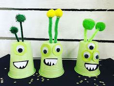 three green plastic cups decorated with monster faces and pom - poms are sitting on a black table