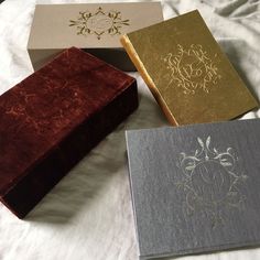 three different colored boxes sitting on top of a white sheet covered bed with decorative designs