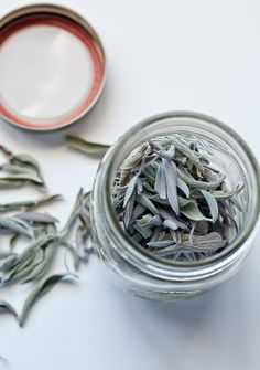 a glass jar filled with dried herbs next to a spoon