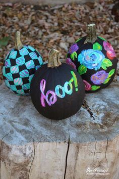 three painted pumpkins sitting on top of a tree stump