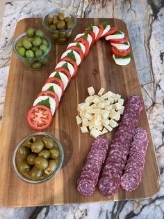 a wooden cutting board topped with olives, cheese and meatsticks on top of a marble counter