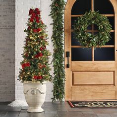 two christmas wreaths are placed next to a potted tree on the front porch