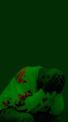 a man sitting on the ground with his head in his hands while wearing a green shirt