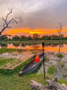 a canoe sitting on top of a lush green field next to a lake at sunset