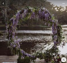 an outdoor wedding setup with purple flowers and greenery on the table next to water