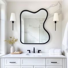 a white bathroom with marble counter top and large mirror over the sink, along with two lamps