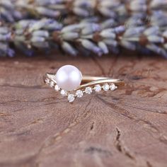 a pearl and diamond ring sitting on top of a piece of wood with lavender flowers in the background