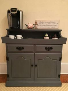 a coffee maker and some cups on top of a gray cabinet in a living room