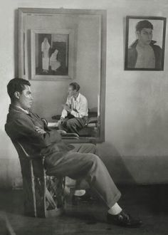 two men are sitting in chairs and one is looking at his reflection on the wall